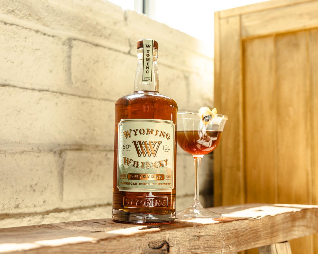 bottle of whiskey and a cocktail on a railing